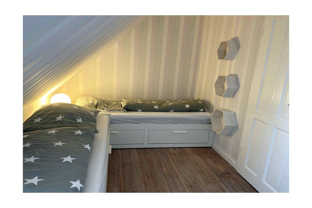Een slaapkamer in loftstijl met een schuine plafond, een bed met sterrenbeddengoed, een nachtkastje en een inbouwkast.