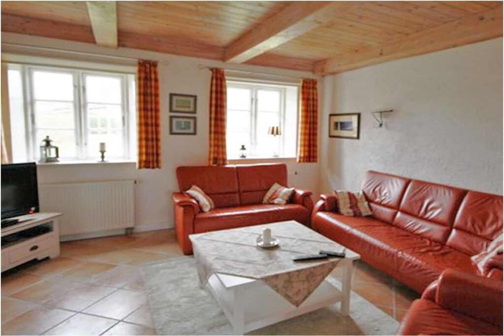 Een woonkamer met een rode bank, een witte salontafel en een televisietoestel op een dressoir.