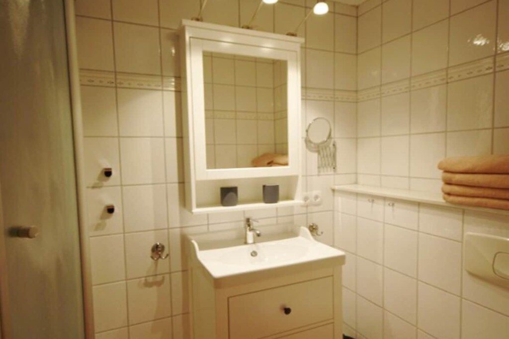 Une salle de bain avec des carreaux blancs, un lavabo, un miroir et un porte-serviettes.