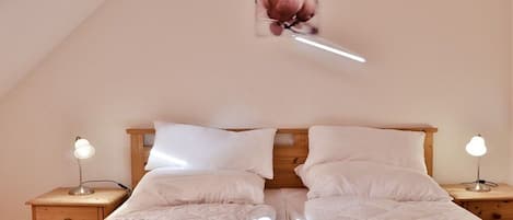 A bedroom with a wooden bed frame, white bedding, two bedside tables with lamps, and a framed picture on the wall.