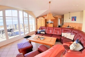 Ein Wohnzimmer mit großem Fenster, einer Sofagarnitur, einem Holztisch und einer Pendelleuchte.