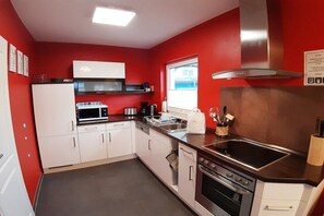 Een kleine keuken met witte kasten, een roestvrijstalen fornuis, een magnetron en een raam voor natuurlijk licht.