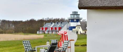 A patio with outdoor seating, a thatched-roof structure, and a view of a lighthouse and buildings in the background.