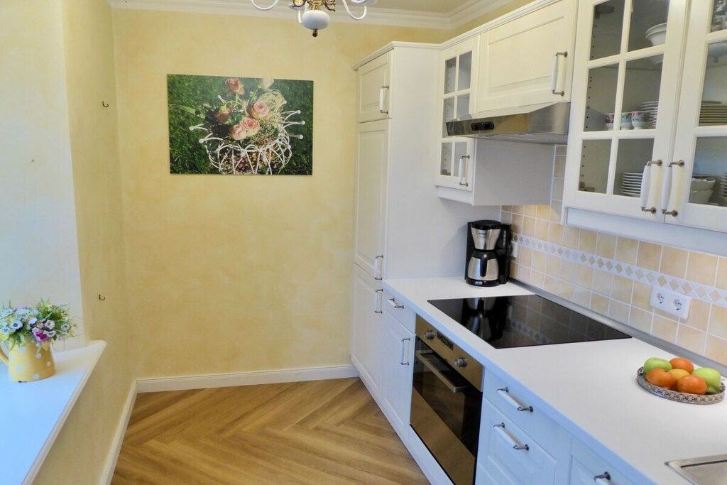 Une cuisine avec des meubles blancs, une cuisinière noire et une machine à café.
