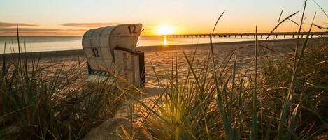 Una silla de playa en la arena, con vista al atardecer y un muelle al fondo.