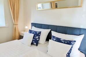 A hotel room with a bed, a nightstand, a lamp, a mirror, and a window with curtains. - Holiday apartment with 1 bedroom (Bastorf OT Hohen Niendorf)