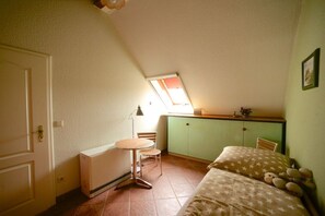 A small, cozy room with a sloped ceiling, a bed with a star-patterned bedspread, a small table with a chair, and a kitchenette area with a window above the sink. - Holiday apartment with 2 bedrooms (Rietz-Neuendorf, OT.Neubrück)