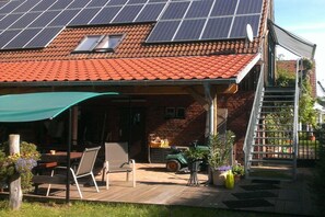 A house with a red-tiled roof, solar panels, a covered patio with furniture, and a brick exterior. - Holiday apartment with 2 bedrooms (Rietz-Neuendorf, OT.Neubrück)