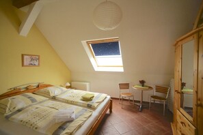 Ein Schlafzimmer mit einem Bett, einem kleinen Tisch, zwei Stühlen, einem Fenster mit Blick zum Himmel und einem Holzschrank.