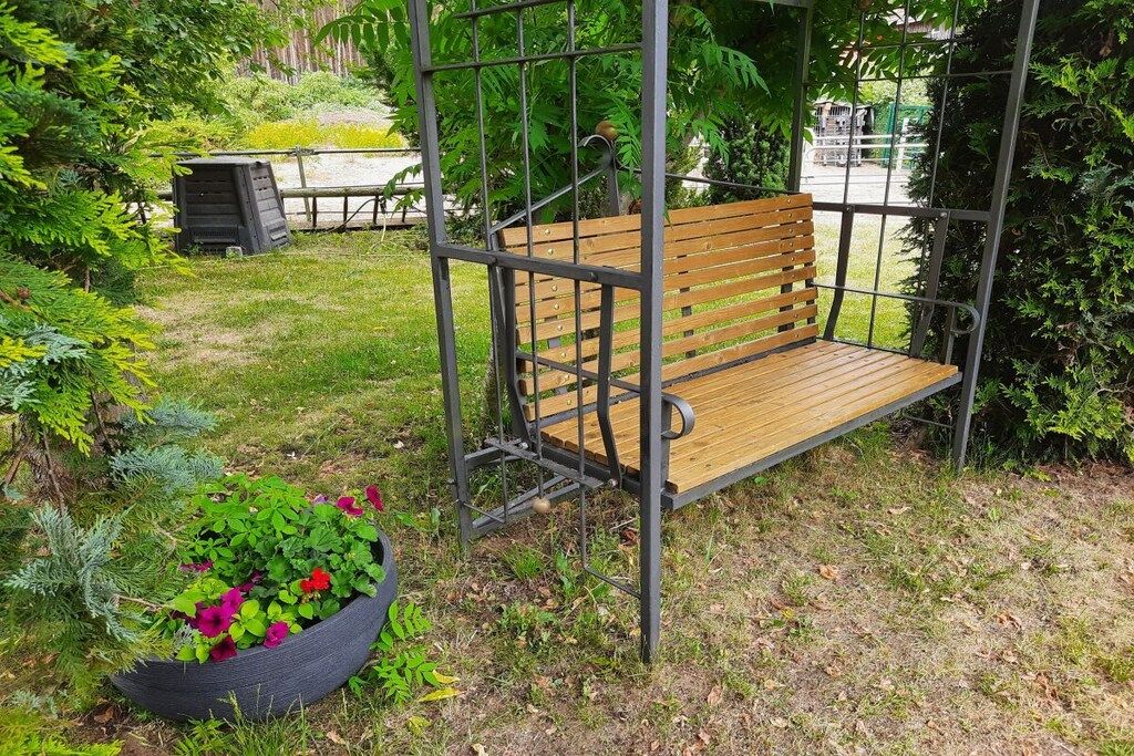 A wooden bench with metal supports, surrounded by greenery and a flower bed.