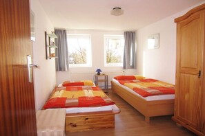 A room with two single beds, a wooden wardrobe, a small table with a lamp, and a window with curtains. - in the Engler holiday home (Högel)