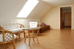 A loft-style room with a sloped ceiling, a glass table, wicker furniture, and a wooden floor. - in the Engler holiday home (Högel)