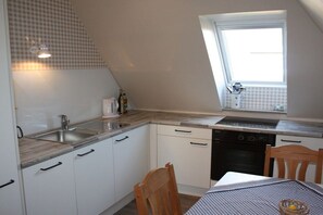 Eine kleine Küche mit Fenster, weißen Schränken, einer Spüle und einem Geschirrspüler.