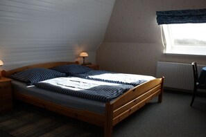 A bedroom with a wooden bed, two bedside tables with lamps, a radiator, and a window with a view. - Holiday apartment with 1 bedroom (Oldsum)