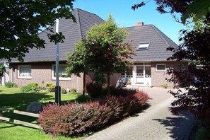 A residential house with a brick facade, a sloped roof, and a paved driveway. - Holiday apartment with 1 bedroom (Oldsum)