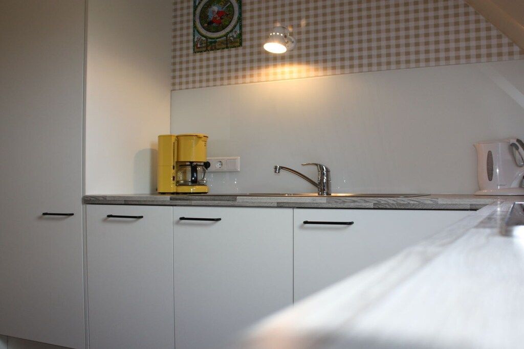 Ett kök med vita skåp, en gul kaffebryggare, en diskho och ett rutmönstrat stänkskydd.