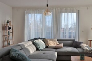 A modern living room with a sectional sofa, a wooden side table, and a hanging light fixture. - Holiday apartment in Bad Doberan with balcony (Bad Doberan)