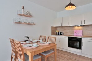 A modern kitchen with white cabinets, a wooden dining table with chairs, and a hanging pendant light. - Holiday apartment in Bad Doberan with balcony (Bad Doberan)