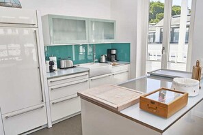 Une cuisine moderne avec des armoires blanches, un pare-feu en verre et une fenêtre donnant sur l’extérieur.