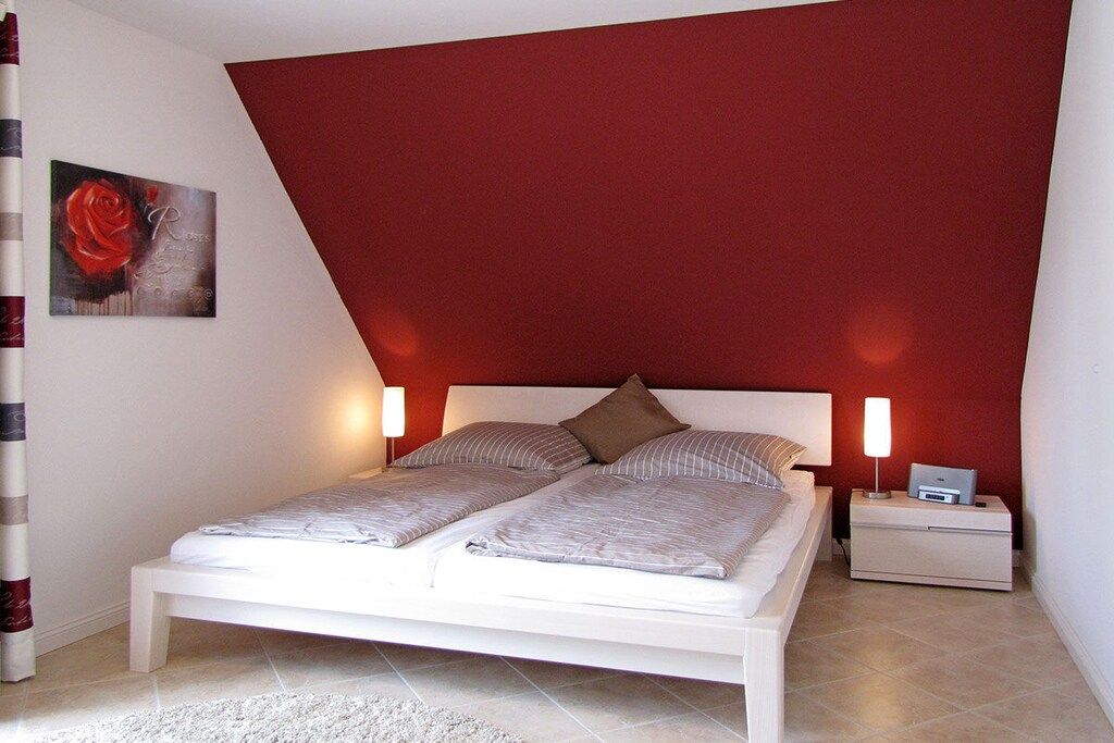 Ein Schlafzimmer mit einem weißen Bett, zwei Nachttischlampen, einem Nachttisch mit einem Drucker und einer roten Akzentwand.