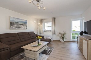 A modern living room with a brown sofa, a wooden coffee table, a painting on the wall, a potted plant, and a TV on a wooden cabinet. - Holiday apartment with 1 bedroom (Sassnitz auf Rügen)