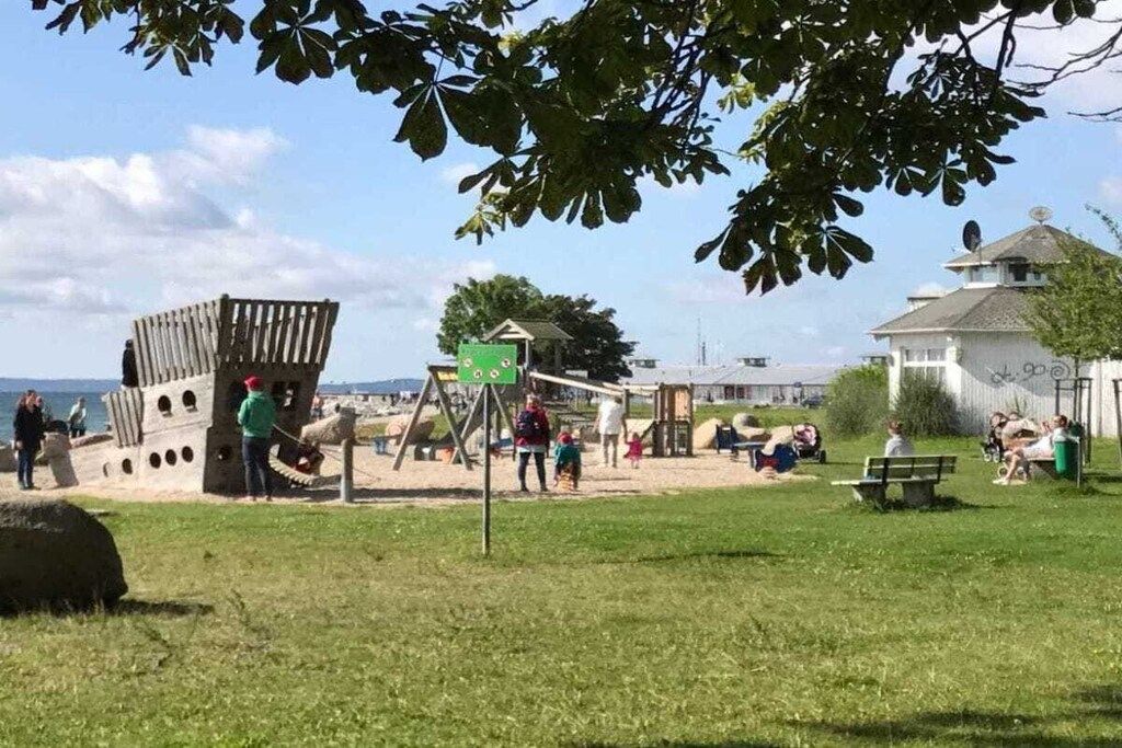 Ein Park mit einem Spielplatz, Bänken und einem Gebäude mit Satellitenschüssel.