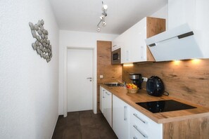 Cuina compacta amb armaris blancs, tauleig de fusta, microones, cafetera i búllet negre.