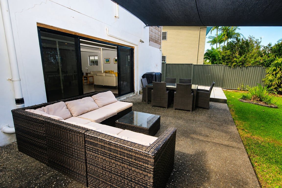 Un espace extérieur aménagé avec un patio, un canapé en osier, une table basse et un ensemble de mobilier de salle à manger.