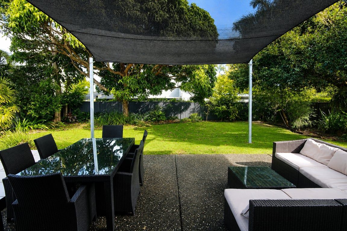 An outdoor patio area with a glass table and chairs, a sofa, and a shaded canopy.