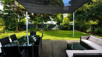 An outdoor patio area with a glass table and chairs, a sofa, and a shaded canopy.