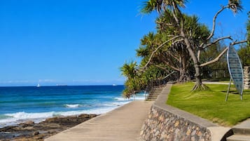 Une promenade en bord de mer offrant une vue sur l’océan, avec un palmier et un panneau indicateur.