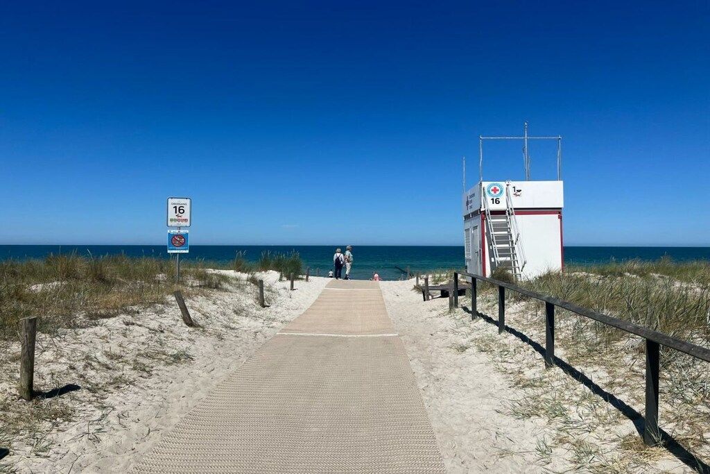 Een strandpad dat leidt naar een uitkijktoren voor strandwachten, met een stoel en een trap.