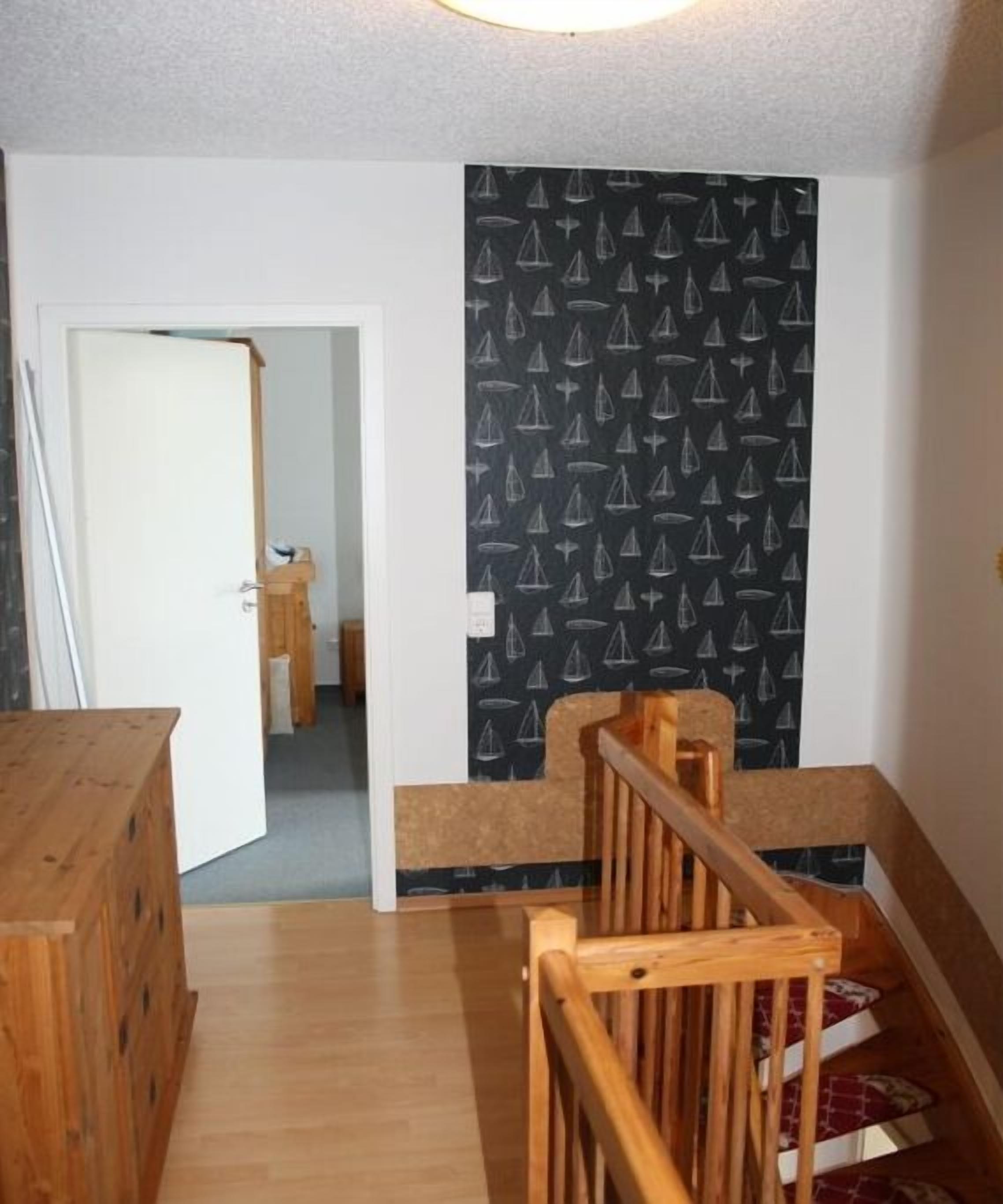 A staircase with a wooden handrail leading to a landing, a door at the top, and a patterned wall.