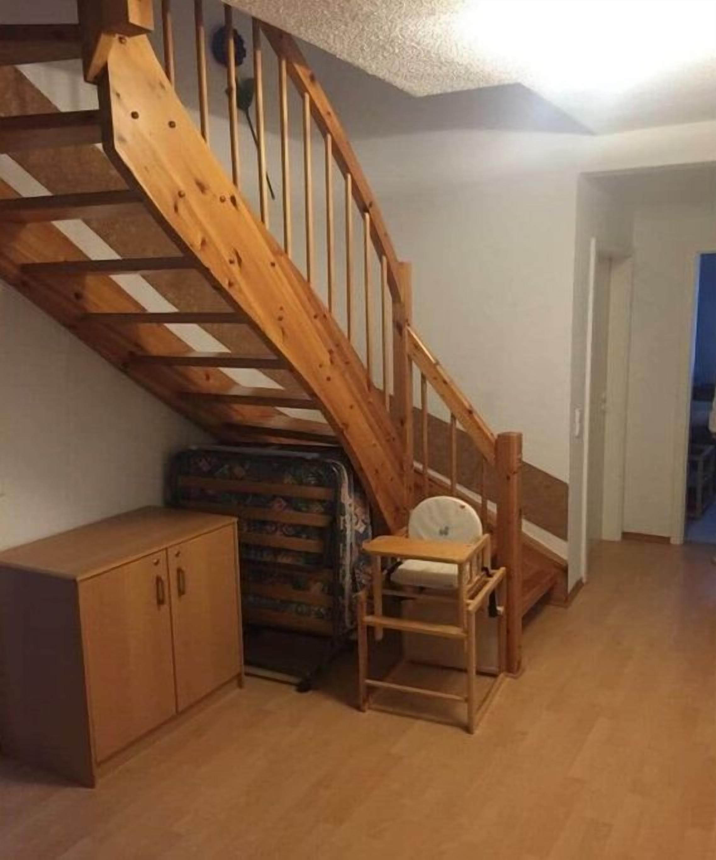 Un escalier en bois menant à un niveau supérieur, une petite chaise en bois et un meuble.