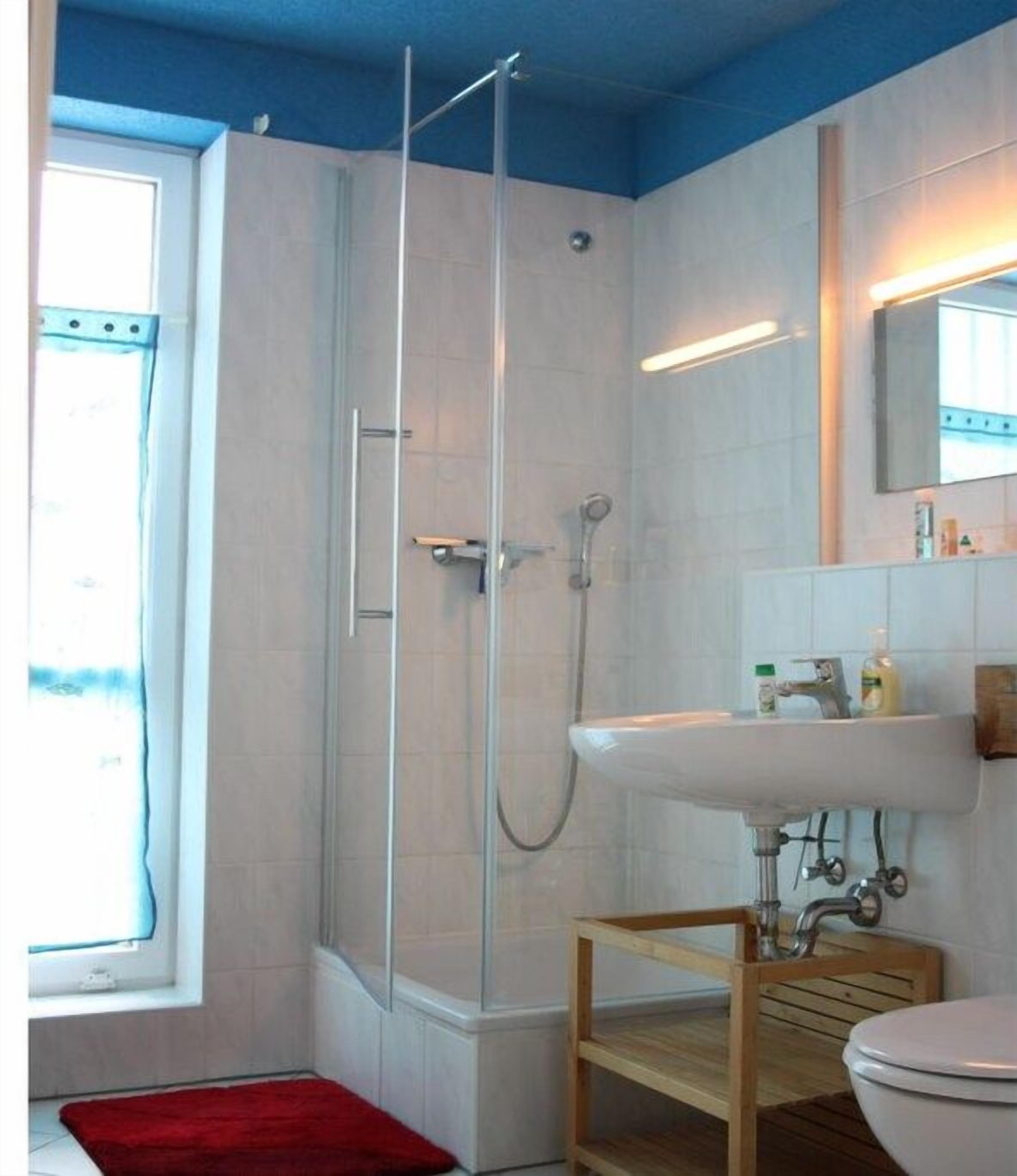 A bathroom with a glass shower enclosure, a white sink, and a wooden shelf.