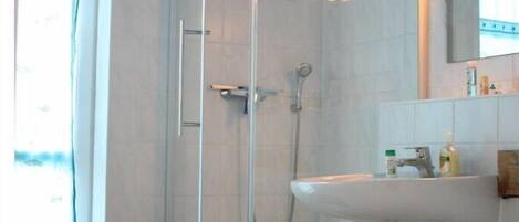 A bathroom with a glass shower enclosure, a white sink, and a wooden shelf.