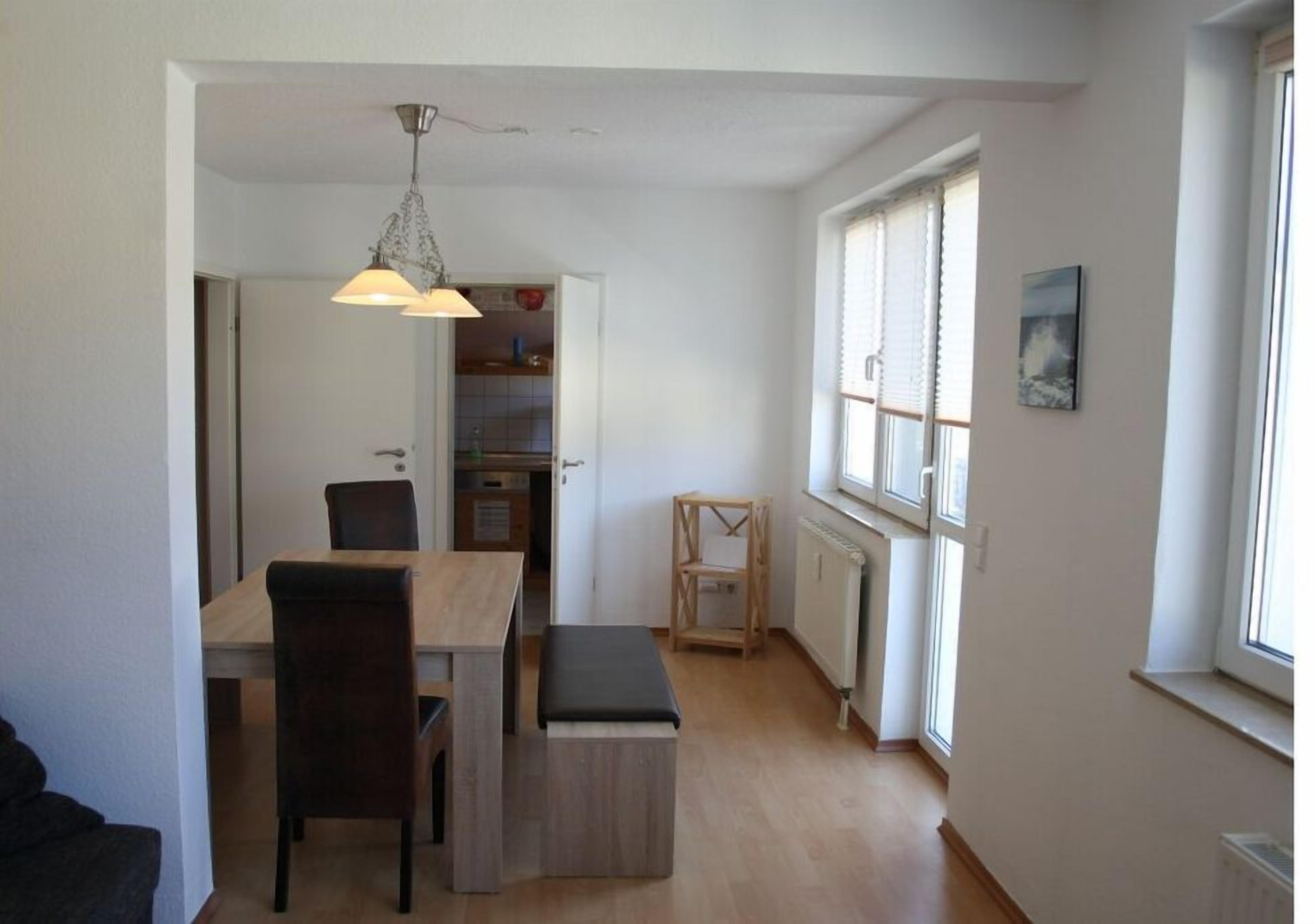A dining area with a table and chairs, a hanging light fixture, a window with blinds, and a radiator.