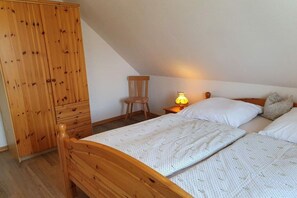 A bedroom with a wooden bed, a nightstand with a lamp, a chair, and a wardrobe. - at Vanessa's House || Zingst (Zingst)