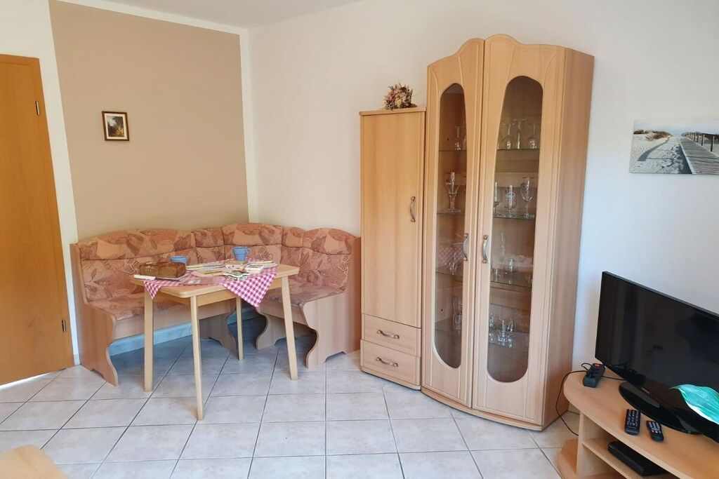 Una sala de estar con un sofá, un mueble de madera con puertas de cristal, un televisor y una mesita con mantel a cuadros.
