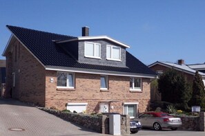 A two-story residential building with a brick facade, a pitched roof, and a car parked in the driveway. - Holiday apartment with 2 bedrooms (Scharbeutz\/Haffkrug)