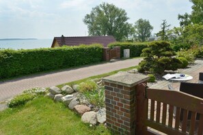 Ein Wohnhaus mit gepflasterter Auffahrt, einer Ziegelmauer, einem Holztor und Blick auf das Meer.