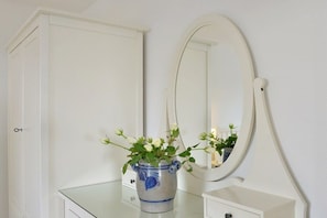 Ein Badezimmer-Waschtisch mit Spiegel, eine Vase mit Blumen und ein weißes Schränkchen.