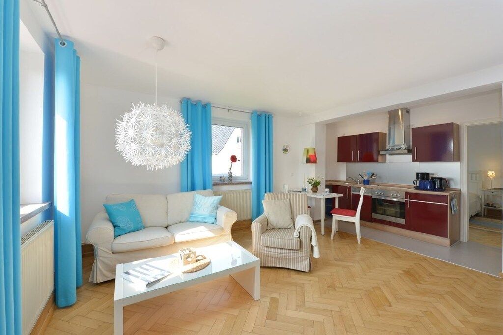 Una sala moderna con sofá, sillón y mesa de centro, comunicada con una cocina que cuenta con armarios y estufa.
