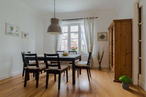 Ein Essbereich mit Holztisch und Stühlen, einer Pendelleuchte, einem Fenster mit Vorhängen und einem Holzschrank.