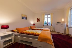 Ein Schlafzimmer mit zwei Betten, einem Nachttisch, einer Kommode und einem Fenster mit Vorhängen.