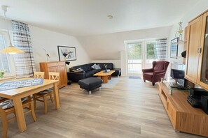 A modern living room with a wooden dining table, black sofa, and a television on a wooden cabinet. - Apartment on the South Beach, Apt. 13 (Wyk auf Föhr)