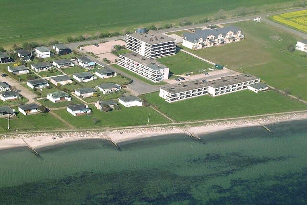 An aerial view of a coastal residential area with multiple buildings, including a large multi-story structure and several single-story houses.