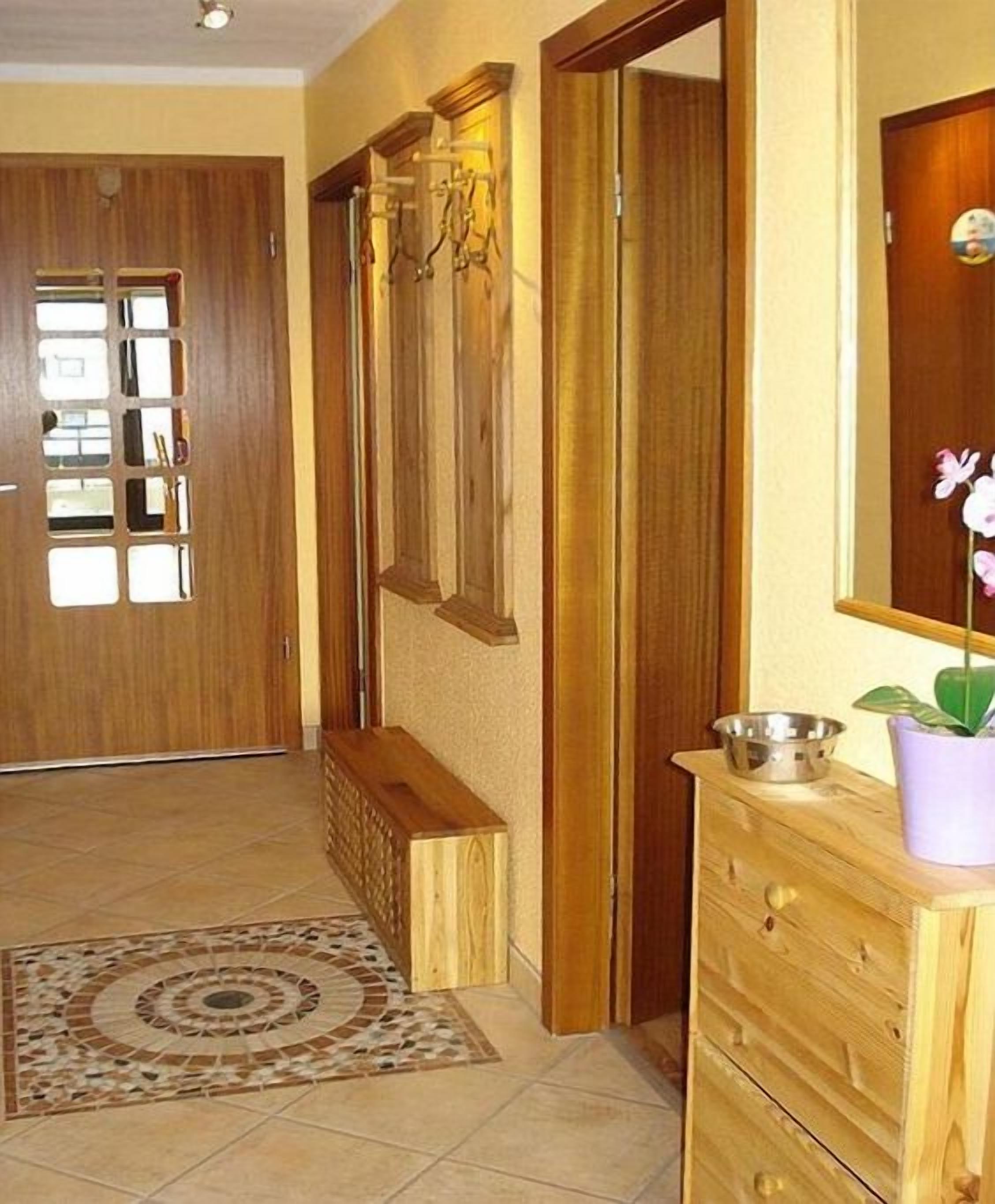 Een houten deur met een ruit, een houten bank, een houten dressoir met spiegel en een potplant.