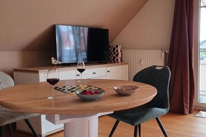 A dining area with a table, chairs, a bowl of fruit, a wine glass, and a television. - Holiday apartment with 1 bedroom (Zingst)