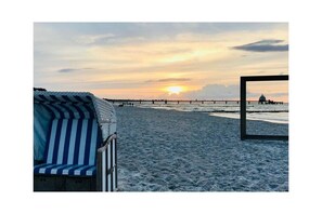 A beach scene with a striped beach chair and a view of the sunset over the water. - Holiday apartment with 1 bedroom (Zingst)